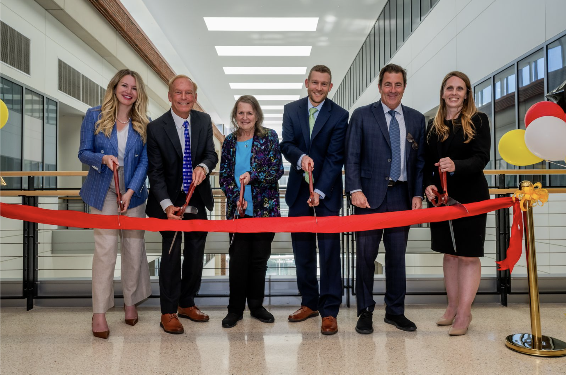6 professionals dressed in business attire cutting a ceremonial ribbon at the University Of Maryland School of Medicine